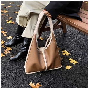 Close-up of brown leather tote bag with white faux shearling trim in a fall park setting