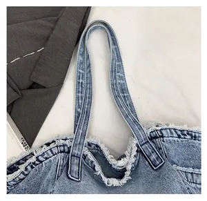 Detail of wide comfortable shoulder strap and distressed edges on washed denim tote bag