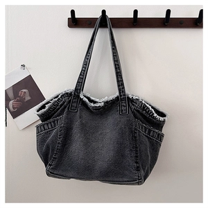 Detail of dark gray washed denim tote bag with raw edges hanging on a wall hook