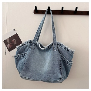 Detail of blue washed denim tote featuring frayed edges and functional multi-pockets
