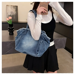 Close-up of vintage washed denim shoulder bag featuring raw fringe edges and side pockets