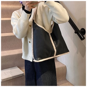 Close-up of black pebble leather tote with cream shearling trim on a model shoulder