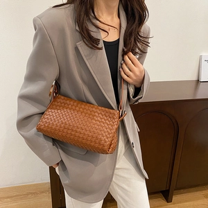 Sac bandoulière minimaliste en cuir tressé marron avec un blazer gris et un pantalon blanc