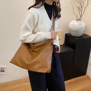 Brown large leather hobo bag for business travel worn by a model in a minimalist setting