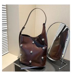 Detail of dark brown leather bucket bag with silver metal rivets and adjustable shoulder strap