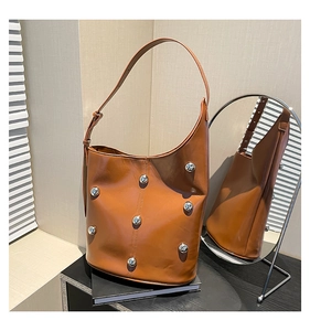 Detail of caramel leather shoulder bag featuring silver metal rivets and a crescent shape