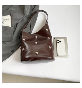 Detail of dark brown rivet shoulder bag with phone for size comparison on white table