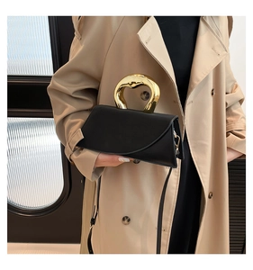 Detail of elegant black leather handbag featuring a unique gold metal handle and slim strap