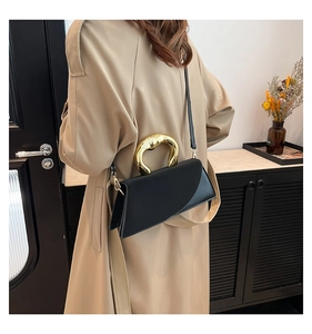 Detail of a geometric black handbag with a sculptural gold handle on a beige trench coat