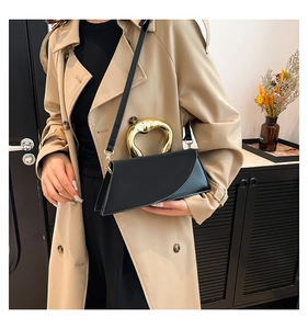 Detail of elegant black crossbody bag with unique gold heart handle on khaki trench coat