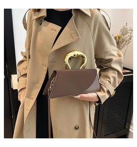 Detail of a dark brown square handbag featuring a unique gold sculpted metal handle