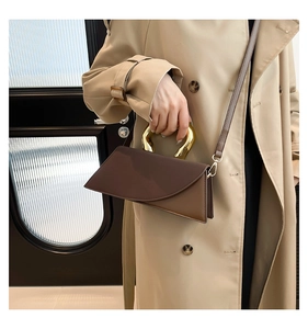 Detail of a chic two-tone brown leather handbag featuring a bold gold-tone metal handle