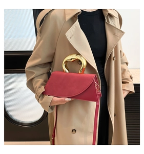 Detail of burgundy square handbag featuring a unique gold metal handle and shoulder strap