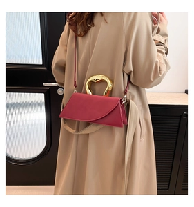 Detail of red leather crossbody bag featuring an asymmetrical design and gold metal handle