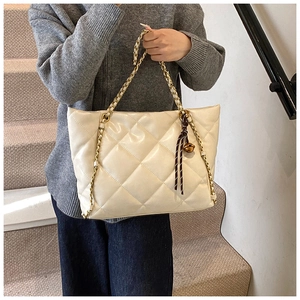Close-up of a cream quilted tote bag with large diamond stitching and a striped tassel charm