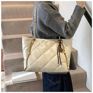 Detail of quilted beige tote bag with gold chain strap and woven rope charm detail