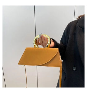 Detail view of mustard yellow leather bag with distinctive gold U-shaped metal handle