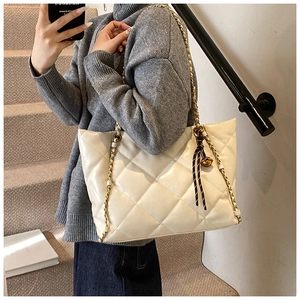 Detail of a beige quilted PU leather tote bag with gold chain strap and tassel charm