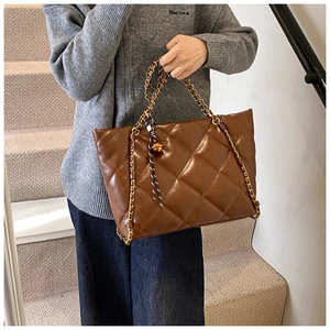 Detailed view of brown quilted tote bag featuring golden metal chain and leather straps