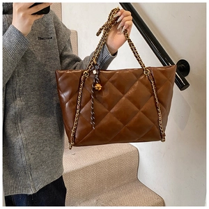 Detailed close-up of brown quilted leather tote bag with gold chain strap in use