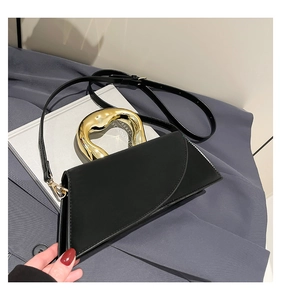 Close-up of black leather handbag with a gold-tone abstract metal handle on a magazine