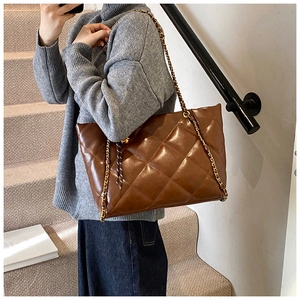 Close-up of quilted brown leather tote bag with gold chain strap on a model's shoulder