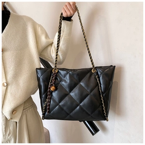 Detail of black quilted tote bag with gold ball charm and chain strap on model shoulder