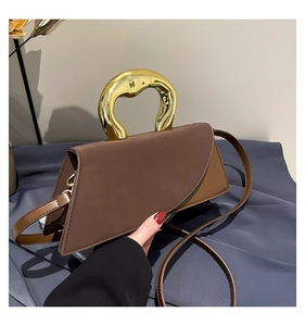 Detail of caramel brown handbag featuring a sculptural gold metal handle and matte texture