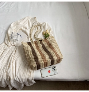 Flat-lay of a striped woven straw tote bag with fringe edge and summer vacation props