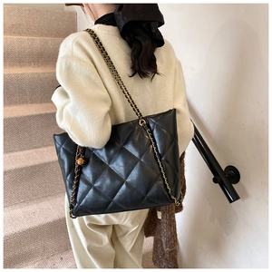 Detail of a black quilted leather tote bag with gold chain strap and metal ball charm