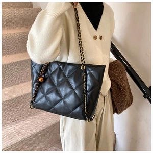 Close-up of quilted leather tote bag featuring gold chain strap and metal ball charm