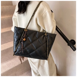 Detail of black quilted tote bag with gold chain strap and metal ball ornament