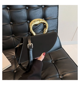 Detail of black geometric handbag featuring a bold liquid gold metal handle and shoulder strap