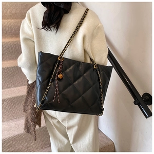 Detail of black quilted tote bag featuring gold chain strap and decorative ball charm