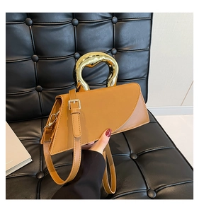 Detail of tan leather handbag featuring a unique gold metal handle and geometric cut