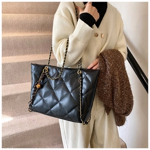Detailed view of black quilted leather tote bag with gold chain strap and metal charm