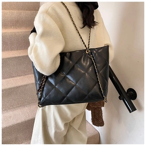 Detail of large black quilted PU leather tote bag with gold metal chain shoulder strap