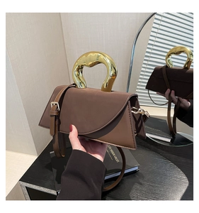 Detail of a brown suede handbag featuring a unique gold organic-shaped metal handle
