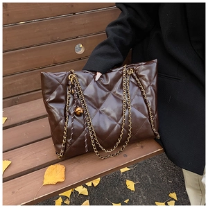 Detail of dark brown quilted leather tote with gold chain strap on autumn bench