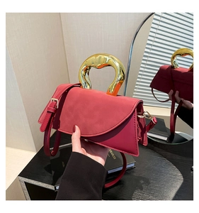 Detail of dark red square bag with unique gold metal handle and removable strap
