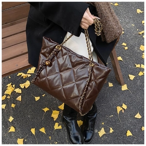 Detail of dark brown quilted tote bag with metal chain strap in autumn outdoor setting