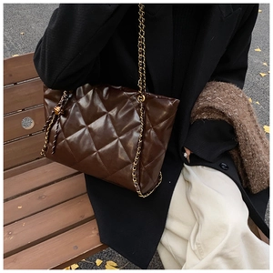 Detail of dark chocolate quilted tote bag with gold chain strap in autumn street setting