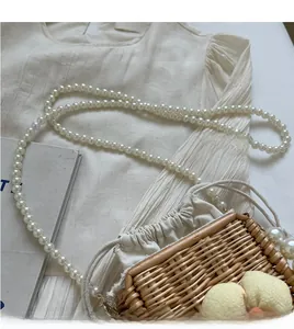 Detailed view of woven straw bag with pearl strap, gold hardware, and drawstring liner