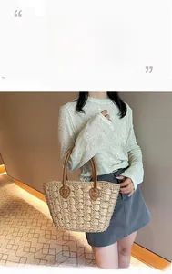 Detail of woven straw tote bag with brown leather handles and white contrast stitching