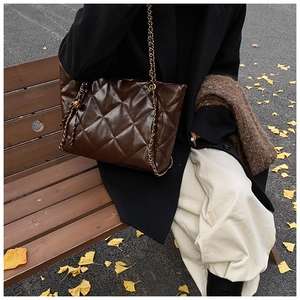 Detail of dark brown quilted tote bag with gold chain strap in an autumn street setting