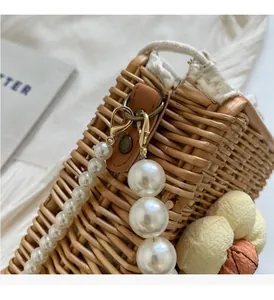 Close-up of woven bag featuring pearl chain strap, floral charms and golden hardware