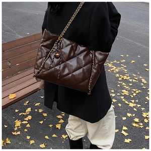 Detail of dark brown quilted tote bag with gold chain strap and metallic ball ornament