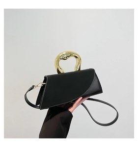 Detail of matte black leather handbag with unique gold sculptural metal handle and flap
