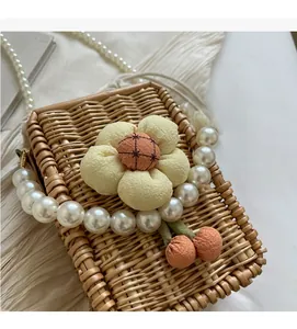Close-up of hand-woven straw bag featuring yellow floral decor and pearl chain strap
