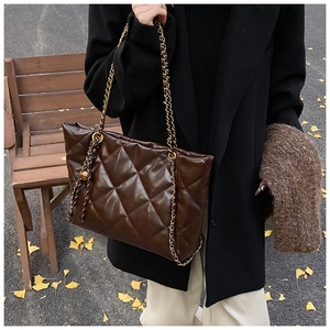 Brown quilted tote bag with chain strap shown on shoulder against autumn leaves